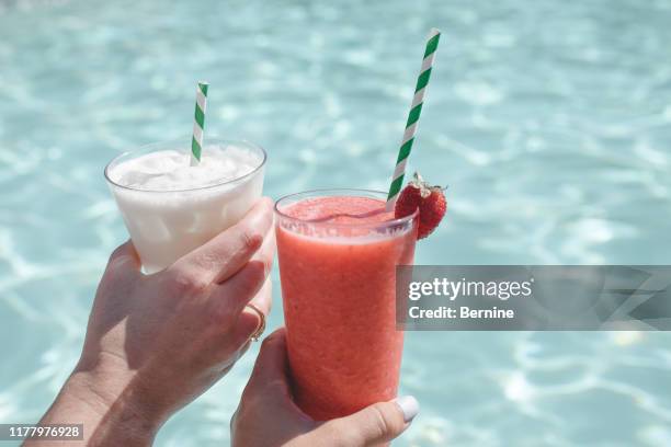 two ladies holding up fruity drinks in front of pool - grooming product stock pictures, royalty-free photos & images