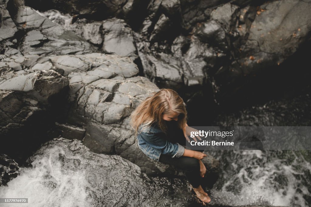 Girl Looking Over Rocks Girl Looking Over A Rocky Cliff With A Waterfall High-Res Stock Photo ...