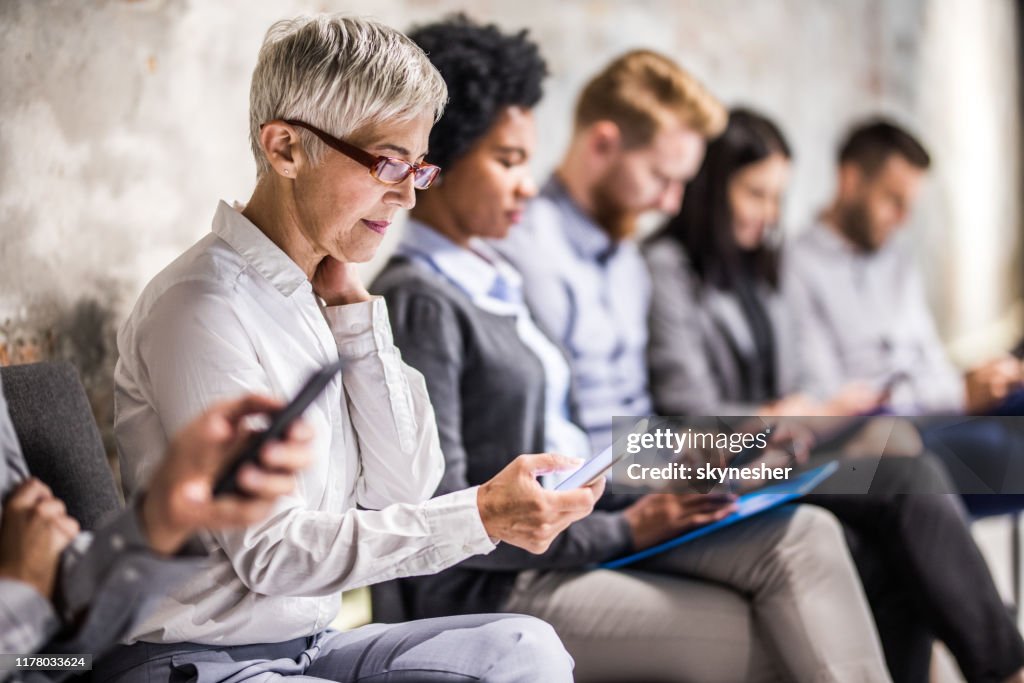 Senior zakenvrouw het gebruik van mobiele telefoon tijdens het wachten op sollicitatiegesprek.