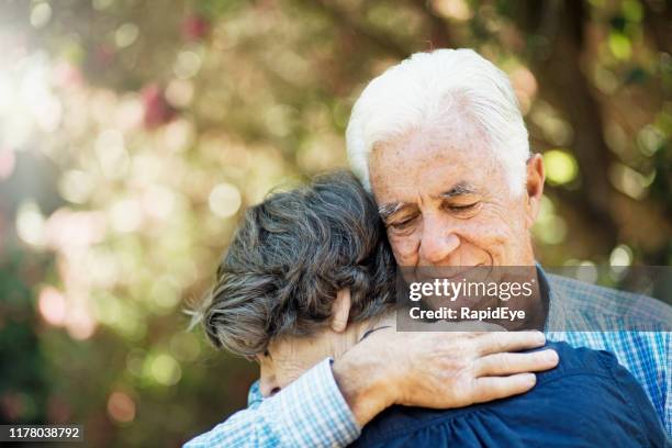 senior paar in aanhankelijk omhelzing in de tuin - compassionate eye stockfoto's en -beelden