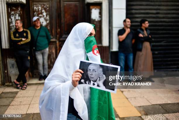 An Algerian protester covering her face with the national flag holds a photo of late leader Mohamed Boudiaf during the 36th consecutive Friday...