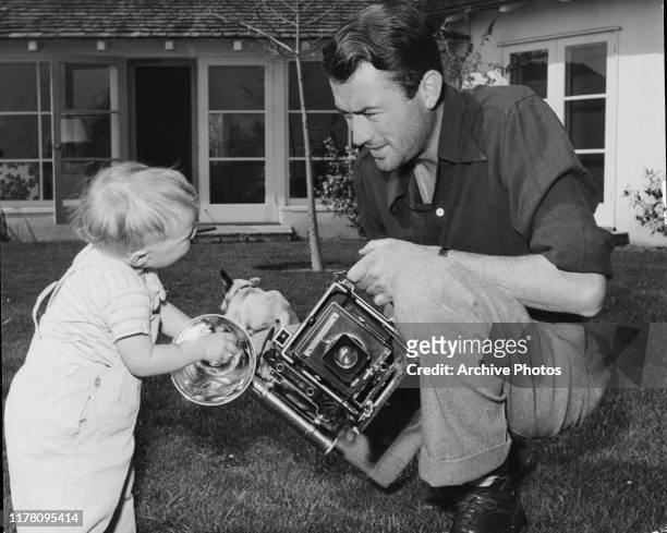 American actor Gregory Peck in his backyard with his two-year-old son Stephen and a Speed Graphic camera which was a gift from his wife Greta, USA,...