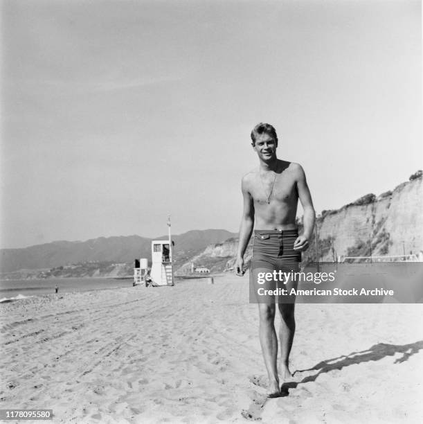 American actor Troy Donahue walking along a beach in swimming trunks, circa 1960.