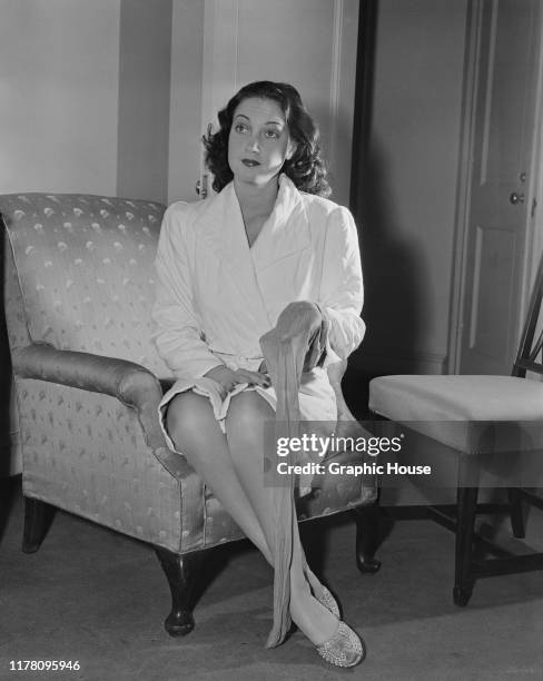 American actress Dorothy Lamour sits in a bathrobe with a single stocking in her hand, circa 1945.