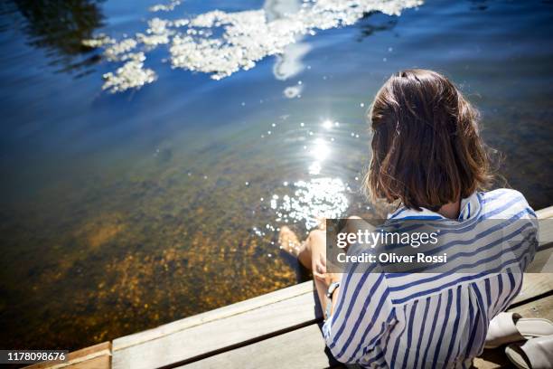 rear view of woman sitting at a pond with feet in water - boardwalk stock-fotos und bilder