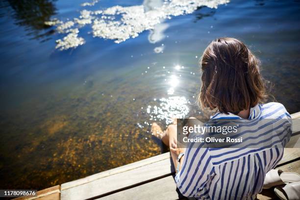 rear view of woman sitting at a pond with feet in water - passerella di legno foto e immagini stock