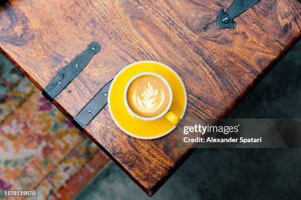 yellow cup of coffee on the table corner, high angle view - coffee table stockfoto's en -beelden