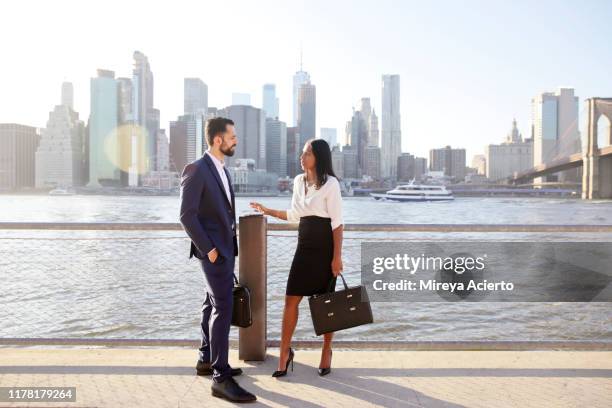 a latinx man and woman of indian ethnicity, wearing business attire, have a conversation in front of the new york city skyline. - panorama nyc day 2 foto e immagini stock