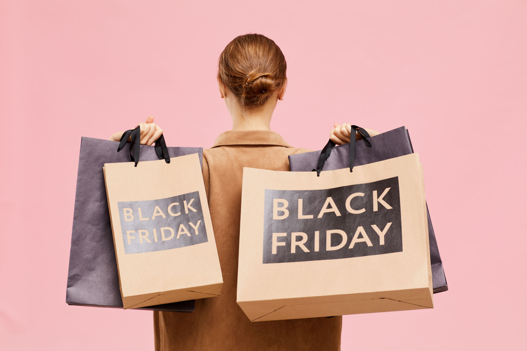 Rear view of unrecognizable woman with hair bun carrying black Friday paperbags on shoulders while leaving store Rear view of unrecognizable woman with hair bun carrying black Friday paperbags on shoulders while leaving store