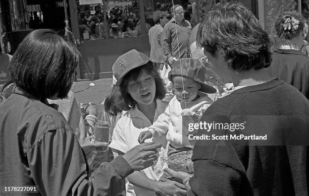 View of a woman with a baby in her arms, alongside others, as they stand on 9th Avenue in Hell's Kitchen during the International Food Festival, New...