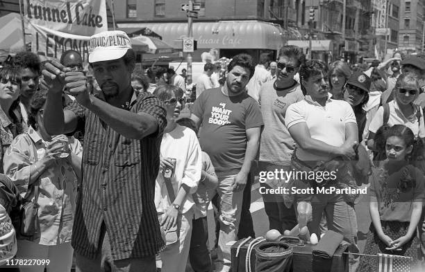 Pedestrians, some with drinks in their hands, watch a street magician perform on 9th Avenue in Hell's Kitchen during the International Food Festival,...