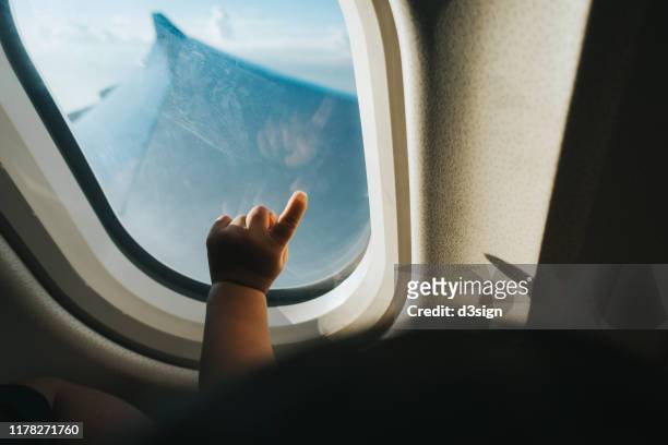 cropped hand of a toddler pointing airplane window against blue sky while travelling - flieger stock-fotos und bilder