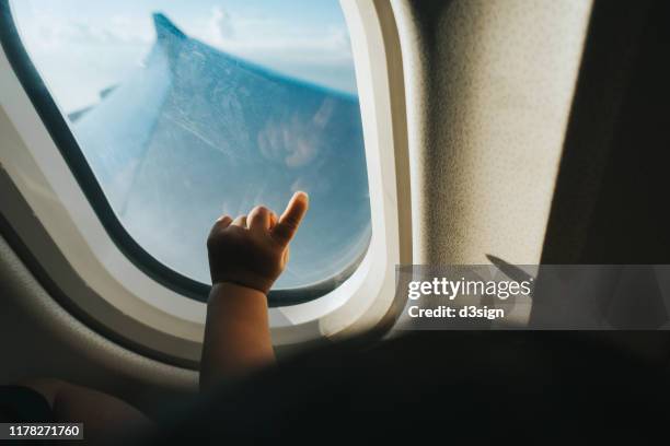 cropped hand of a toddler pointing airplane window against blue sky while travelling - baby imagination stock pictures, royalty-free photos & images