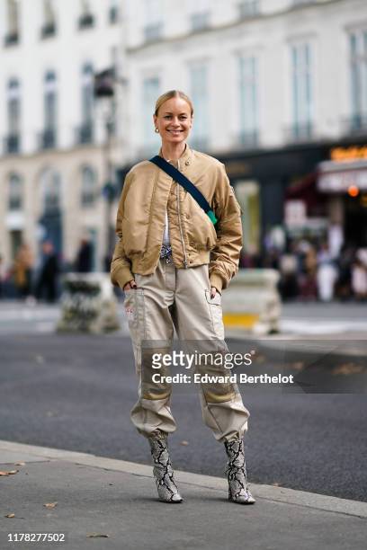 Thora Valdimars wears a cream color bomber jacket, a shoulder strapped bag, gray pants with cargo pockets, snake print pattern boots, outside...