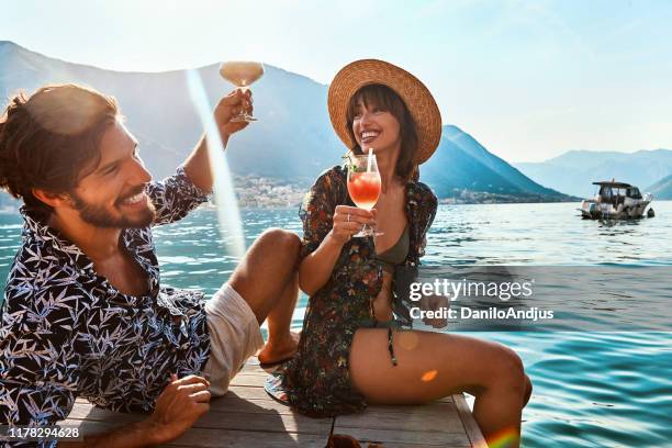 happy couple on honeymoon vacation drinking cocktails by the sea - tropical beach couple stock pictures, royalty-free photos & images