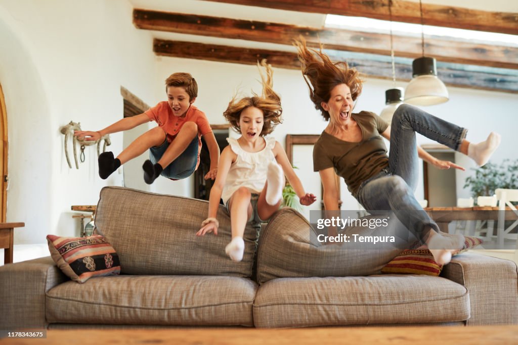Rennen um den besten Platz auf dem Sofa. Mutter und Kinder springen.