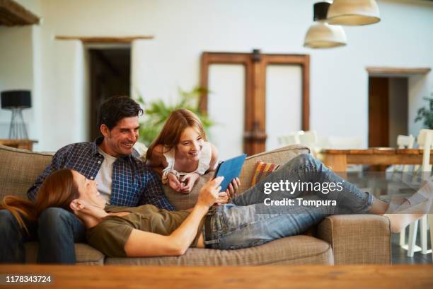 family at home sharing a digital tablet and relaxing on the sofa. - family at home stock pictures, royalty-free photos & images