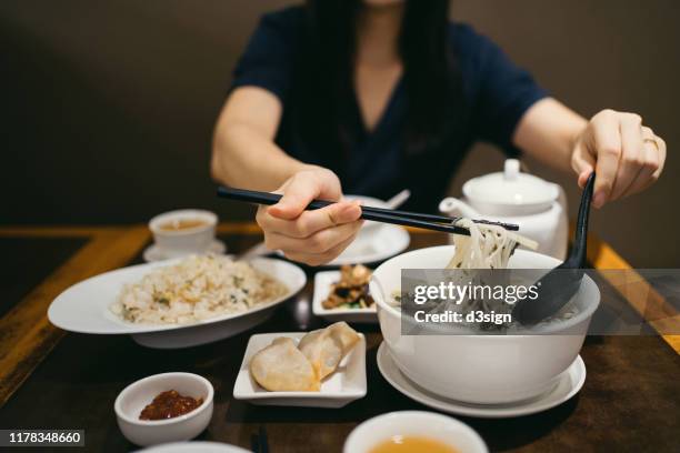 midsection of young asian woman having a bowl of soup noodle and enjoying a variety of dishes in a chinese restaurant - noodle soup stock pictures, royalty-free photos & images