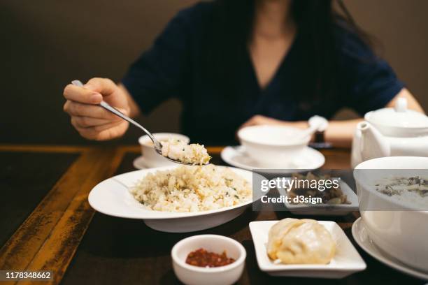 midsection of young asian woman eating and sharing fried rice and a variety of dishes in a chinese restaurant - gebakken rijst stockfoto's en -beelden