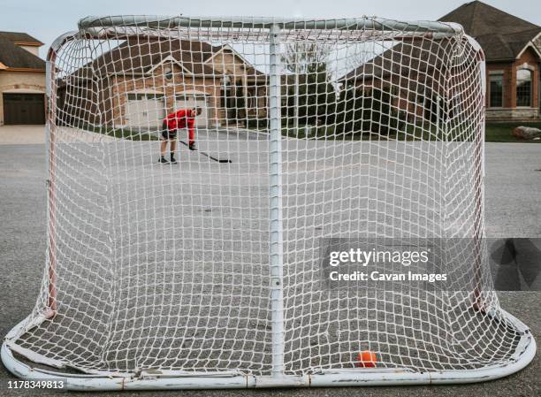 tween boy shooting a ball into hockey net outside on the street. - hockey net stock pictures, royalty-free photos & images