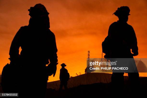 Members of an inmate firefighting crew are silhouetted against a hillside with a track of PG&E lines during firefighting operations to battle the...