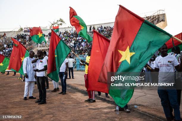 People hold Burkina Faso flags during a meeting to support national security and defence forces, in Ouagadougou's municipal stadium, on October 26,...