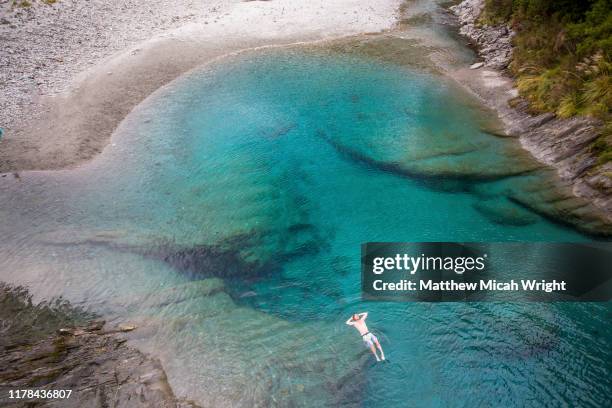 the blue pools of makarora offer enticing blue waters to swim in. a man jumps off a bridge into the water. - den sprung wagen stock-fotos und bilder