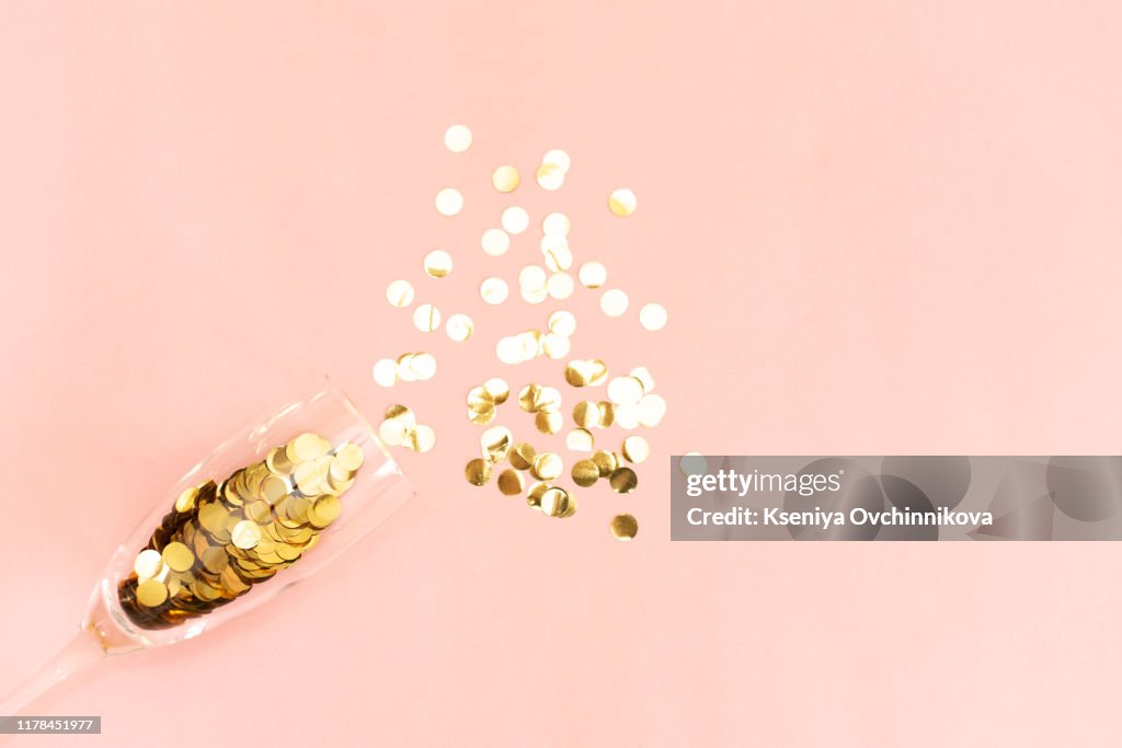 Star-shaped silver confetti poured out of champagne glass on pink background with copy space for text. Top view. Holiday and celebration concept.