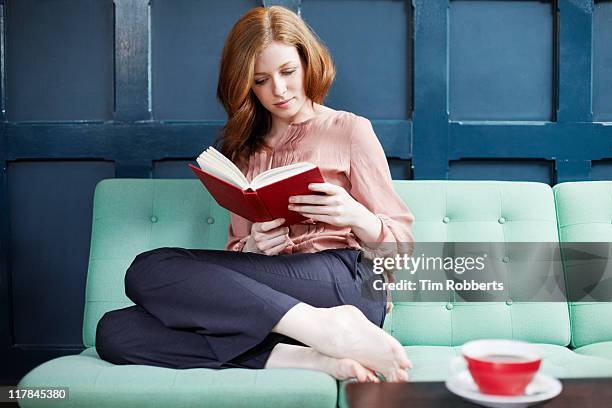 woman reading a book on sofa. - leggere foto e immagini stock