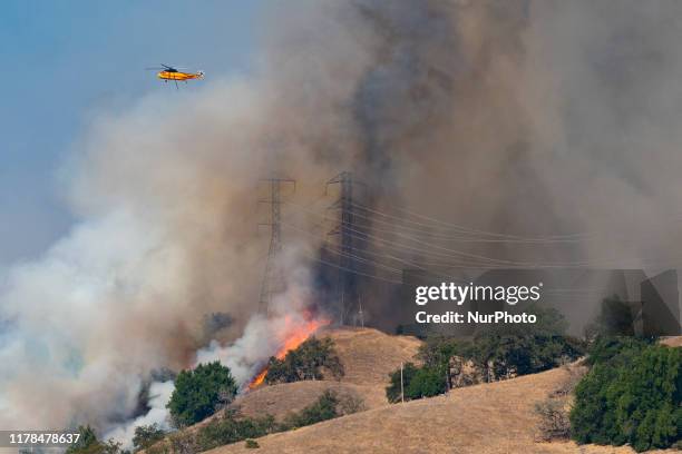 Fire fighting helicopter flies over the power transmission towers, which are engulfed in back fire set by the firefighters in an effort to control...