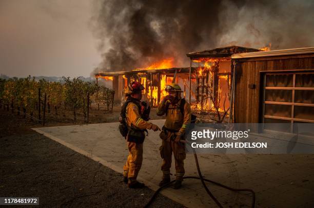 Firefighters discuss how to approach the scene as a home burns near grape vines during the Kincade fire in Healdsburg, California on October 27,...