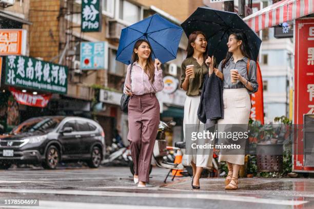 fröhliche freundinnen zu fuß auf der stadtstraße mit regenschirm und kaffee - enjoy monsoon stock-fotos und bilder
