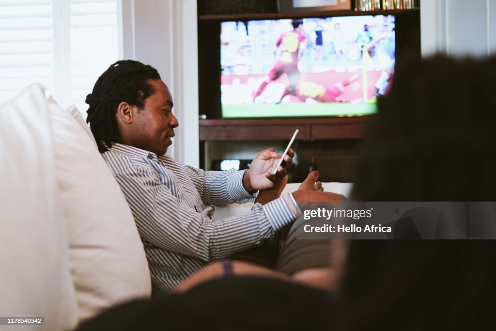 Father texting whilst mother watches sport on TV