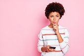 Photo of pretty dark skin lady holding telephone deciding what comment to write hand touch chin wear white striped pullover isolated pastel pink color background