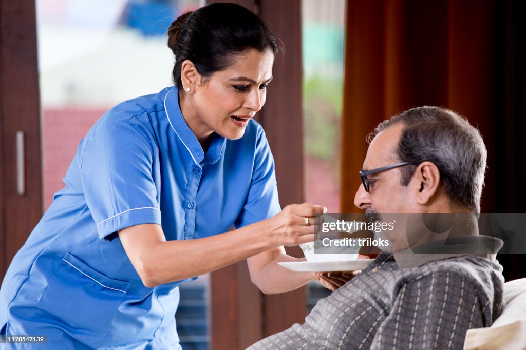Nurse feeding food to old man on bed