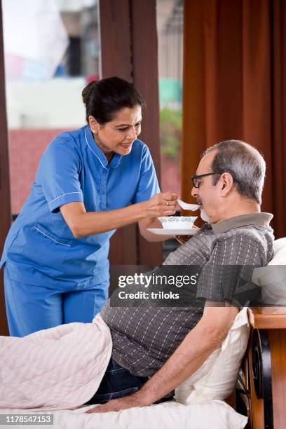 nurse feeding food to old man on bed - hospital food service stock pictures, royalty-free photos & images
