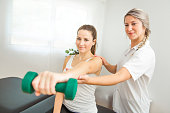 A Modern rehabilitation physiotherapist at work with client. Working on shoulder with dumbell