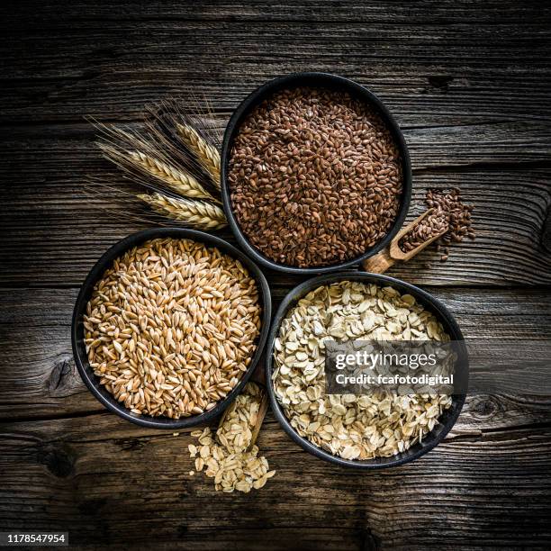 fibra alimentare: farro, fiocchi d'avena e semi di lino girati su un tavolo rustico in legno - cereali da colazione foto e immagini stock