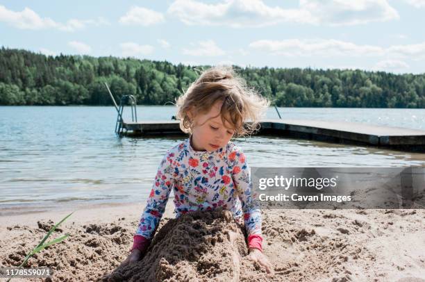 young girl playing in the sand at the beach - girl blowing sand stock-fotos und bilder