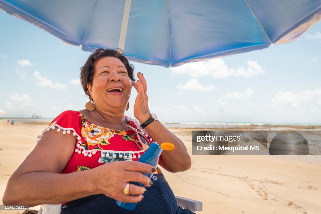 Mujer mayor usando una loción bronceadora en la playa
