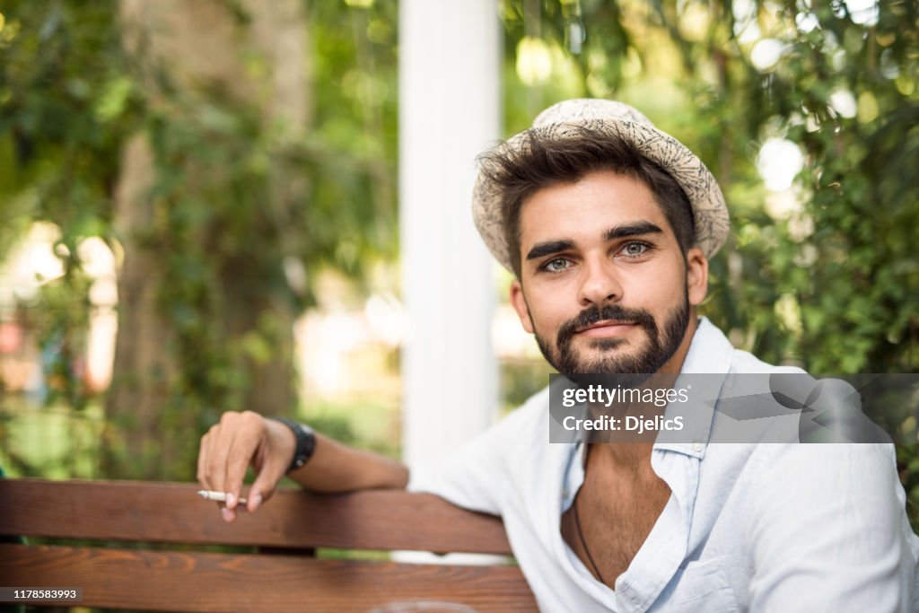 Jeune homme fumant une cigarette à l'extérieur.
