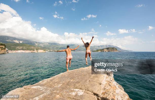 young adventurous couple cliff jumping into beautiful sea. - cliff dive stock pictures, royalty-free photos & images