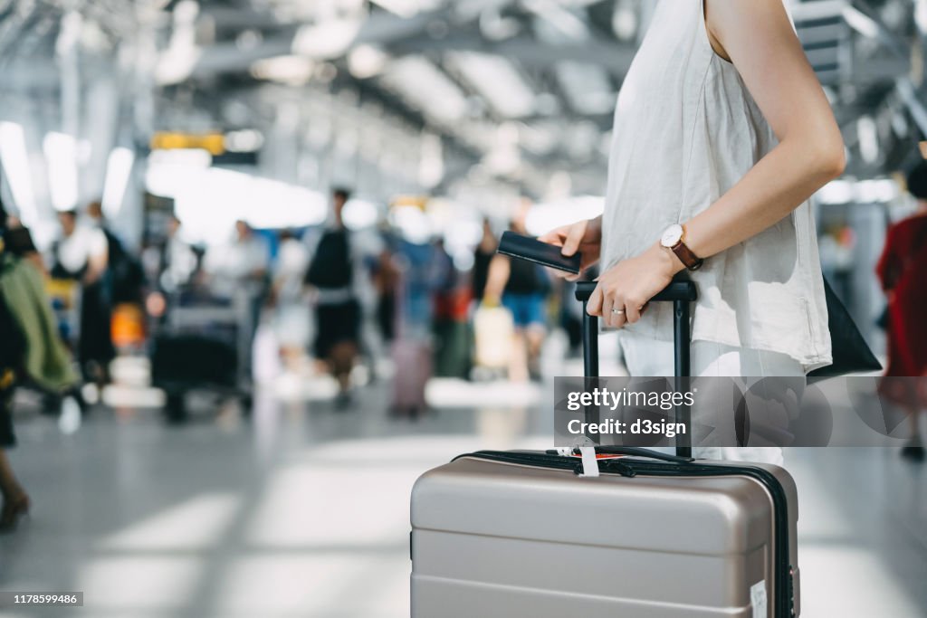 Cropped image of young woman holding passport and suitcase walking in the international airport hall