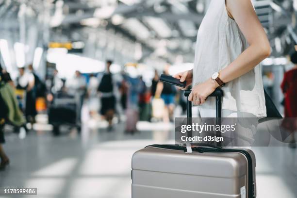 cropped image of young woman holding passport and suitcase walking in the international airport hall - bagagem imagens e fotografias de stock