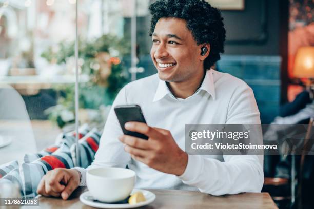 portrait of modern man with wireless earbuds in a cafe - in ear headphones stock pictures, royalty-free photos & images