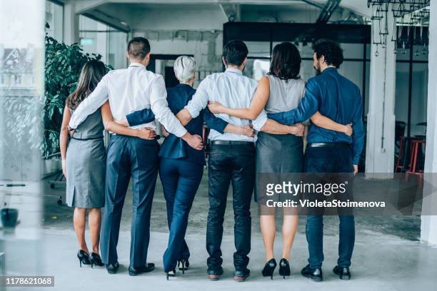 rear view of a business team standing together - arms around stock pictures, royalty-free photos & images