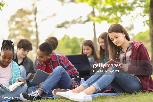 multi-ethnic group of teenagers at park with friends. - teenagers reading books stock pictures, royalty-free photos & images