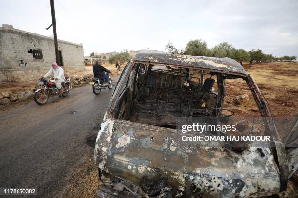 Picture taken on October 28, 2019 shows Syrian bikers riding past a damaged car at the site of a suspected US-led operation against Islamic State...