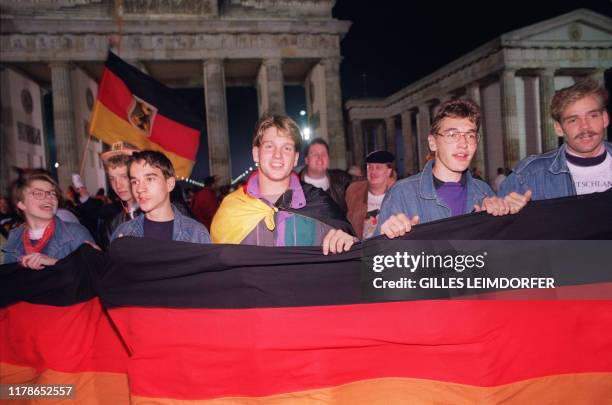 Berliner youths hold and wave German flags as they celebrate the country's reunification at the Brandenburg Gate in Berlin 03 October 1990....