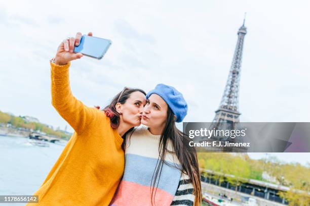 two women taking a selfie with smart phone in front of the eiffel tower - photos of lesbians kissing stock pictures, royalty-free photos & images